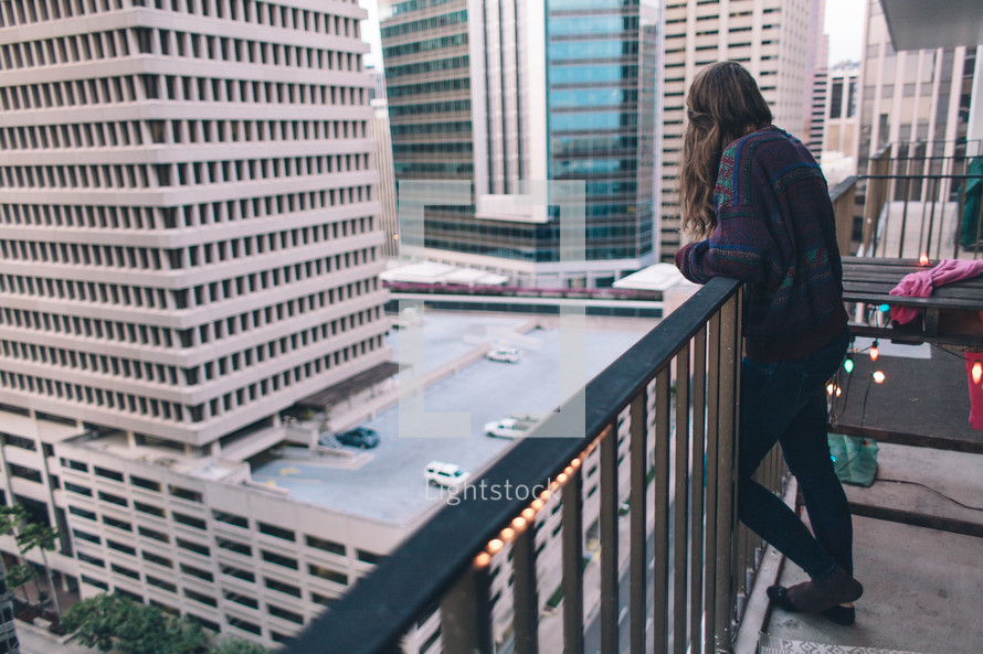 woman standing on a balcony looking out at the city below 
