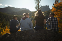young adults sitting on a rock looking out at a lake in fall 
