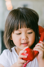 little girl talking on a red telephone 