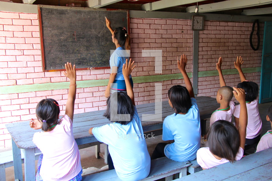 students with raised hands in a classroom 