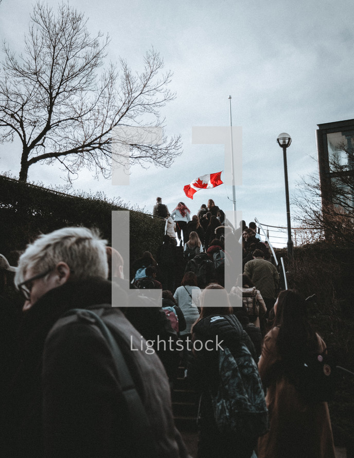 people walking up stairs outdoors under a Canadian flag 