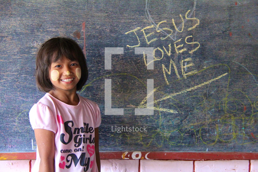 Jesus loves me on a chalkboard pointing to you a young girl in Myanmar