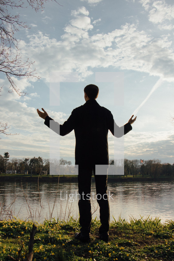 a man standing on a lake shore with raised hands 