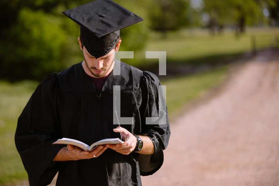 Graduate standing outdoors reading the Bible.