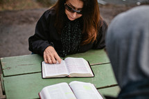 Woman reading an open Bible on a picnic table.