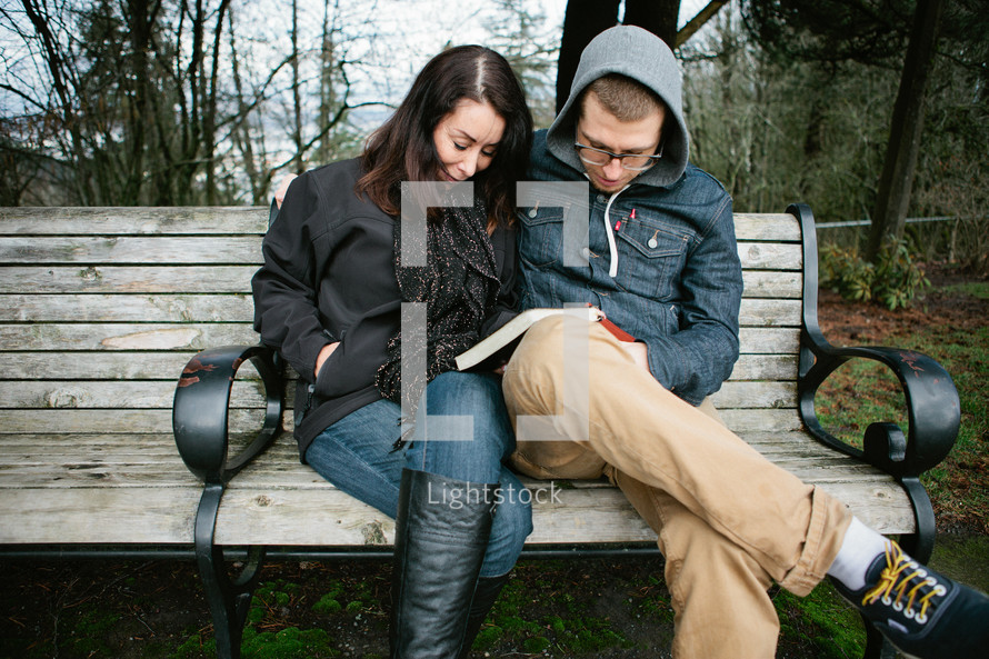 Mother and son praying together over a Bible, while sitting outside on a park bench.