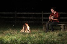 man playing a guitar by a campfire 