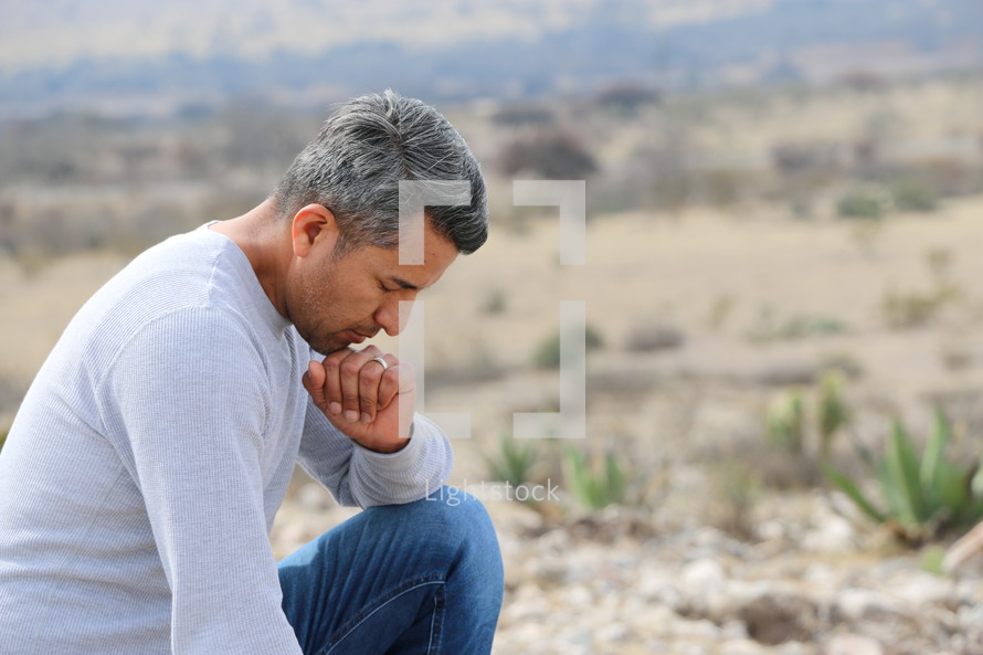 a man kneeling in prayer in a desert 