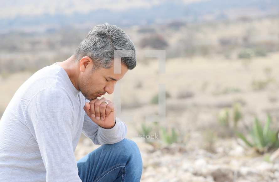a man kneeling in prayer in a desert 