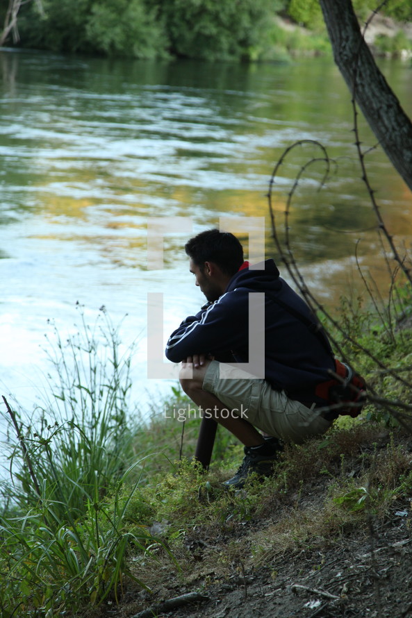 man squatting on a river bank