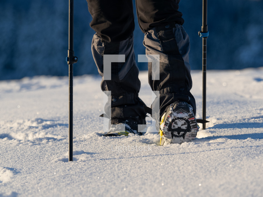Close up of a man hiking on a mountain covered on snow, in boots with shoe skpikes. Outdoor winter trekking