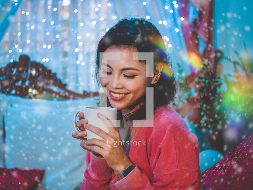 a smiling woman holding a mug surrounded by bokeh lights 