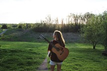 a girl with a guitar on a her back walking outdoors 