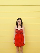 woman standing in a red dress against a yellow wall 