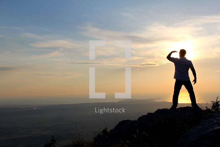 a man looking out at the view standing on a mountain top at sunrise/sunset