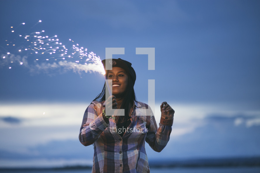 A smiling woman holding a fiery sparkler.