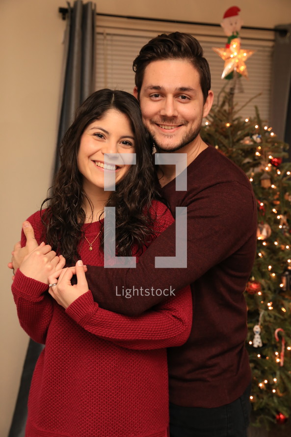 a couple snuggling in front of a Christmas tree 