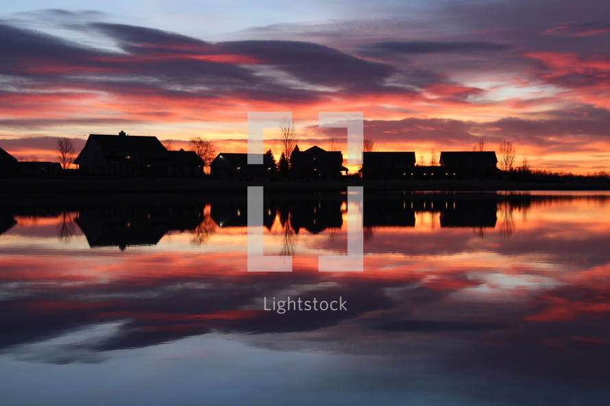 silhouettes of houses across a pond at sunset 