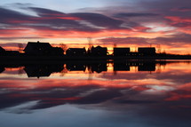 silhouettes of houses across a pond at sunset 