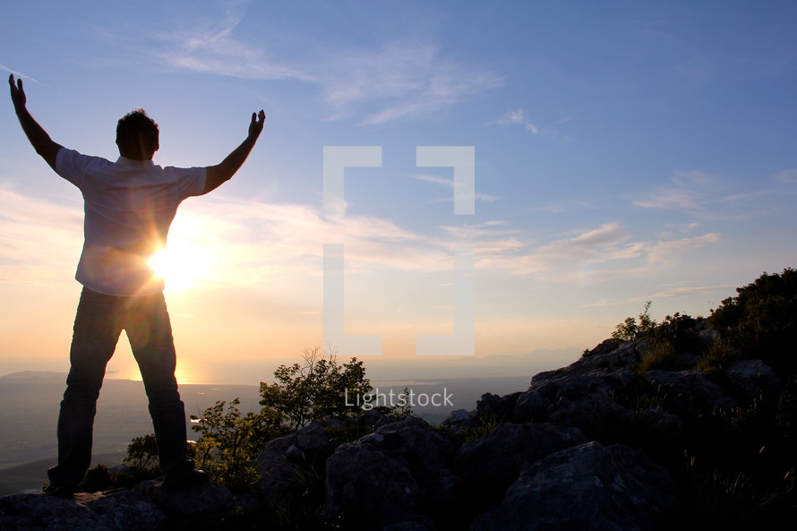 a man with raised hands standing on a mountain top praising God