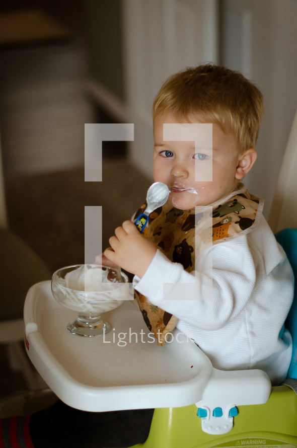 a toddler boy eating yogurt in a highchair 