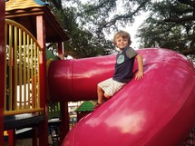 A young boy sits on a pink slide.