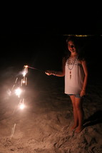 A little girl holding a sparkler on a beach 