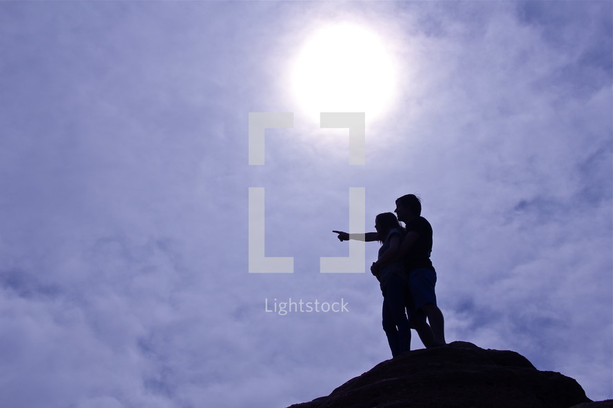silhouette of a couple pointing standing on top of a mountain 