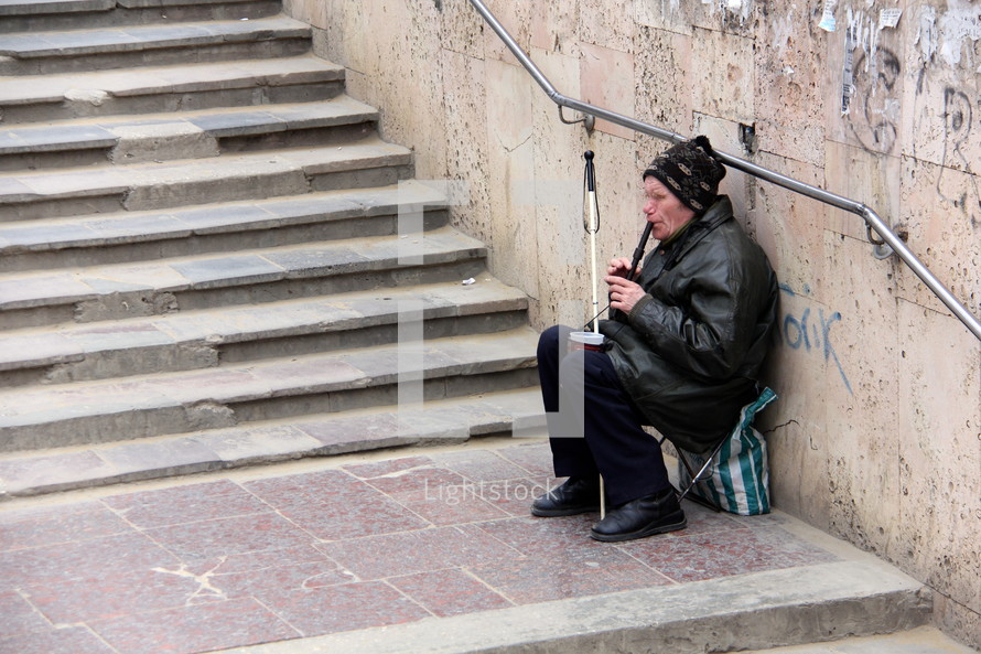 A blind man playing a recorder on stone steps for money