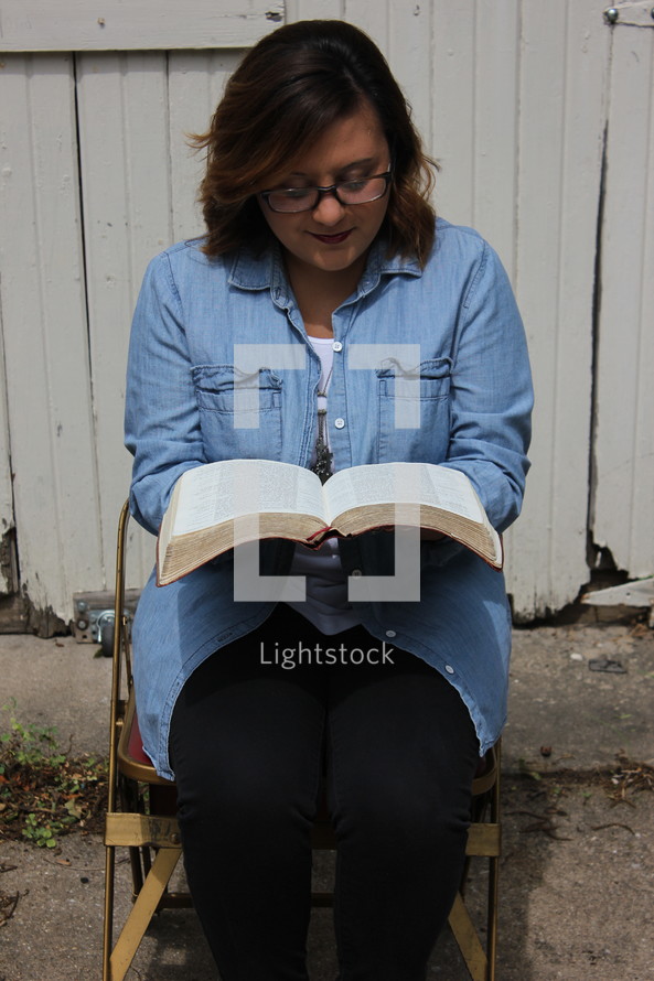 a woman sitting in a chair reading a Bible 