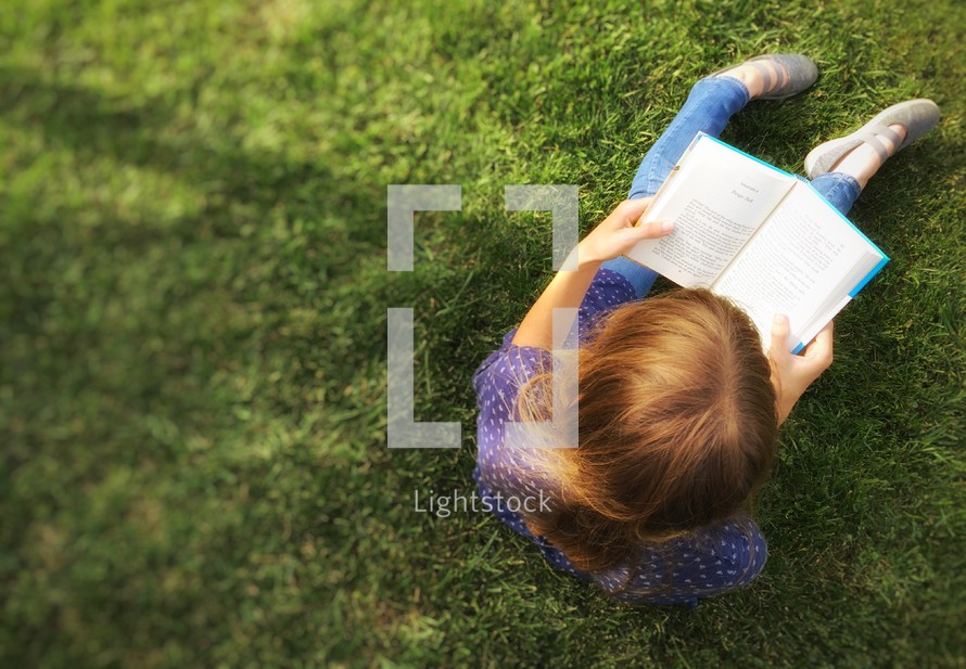 a girl reading a Book in grass