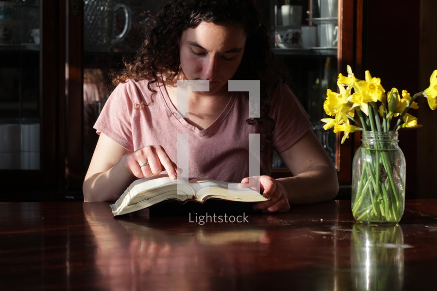 young woman sitting at a table reading a Bible 