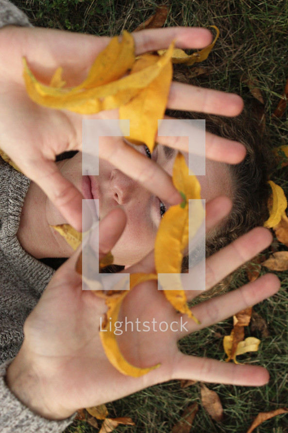 girl lying in the grass playing with fall leaves 