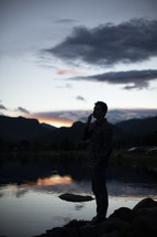a man standing alone at the edge of a pond thinking and praying 