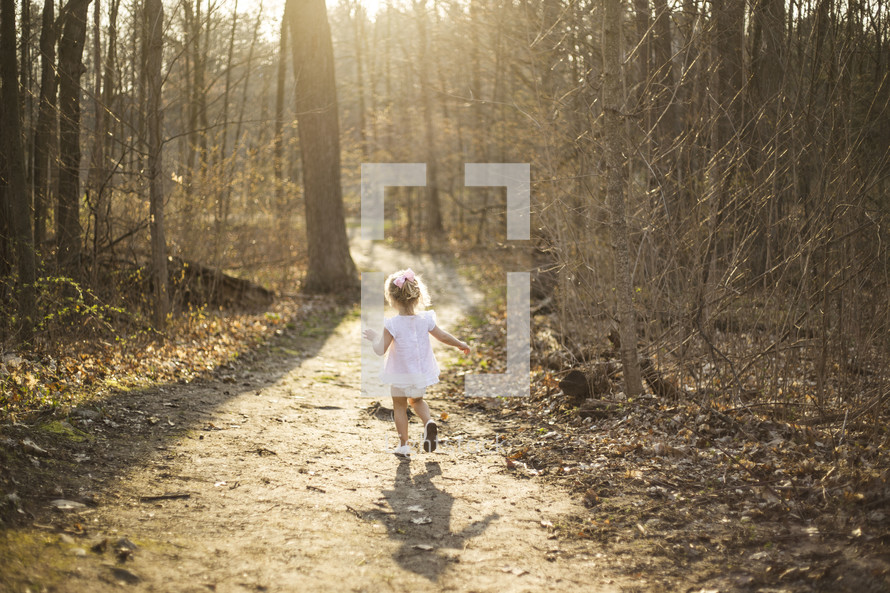 a toddler girl running on a path in the woods 