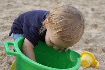 A child plays with a toy bucket on a sandy beach.