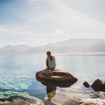 a woman sitting on a rock by a lake 