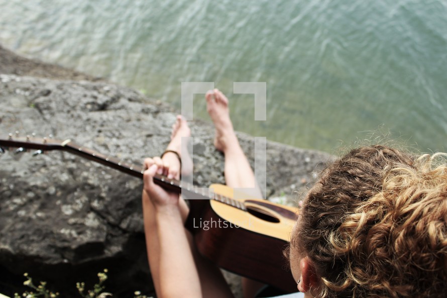 a girl playing an acoustic guitar sitting on a shore 