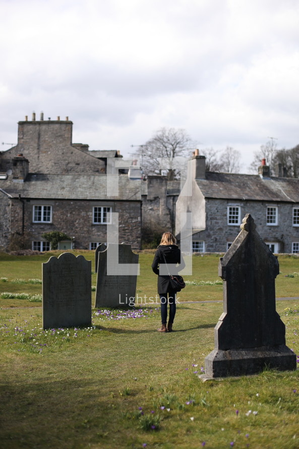 A woman walks away from a cemetery near a stone church.