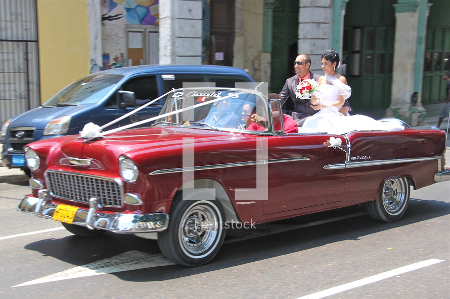 Bride and groom riding in a red convertible.