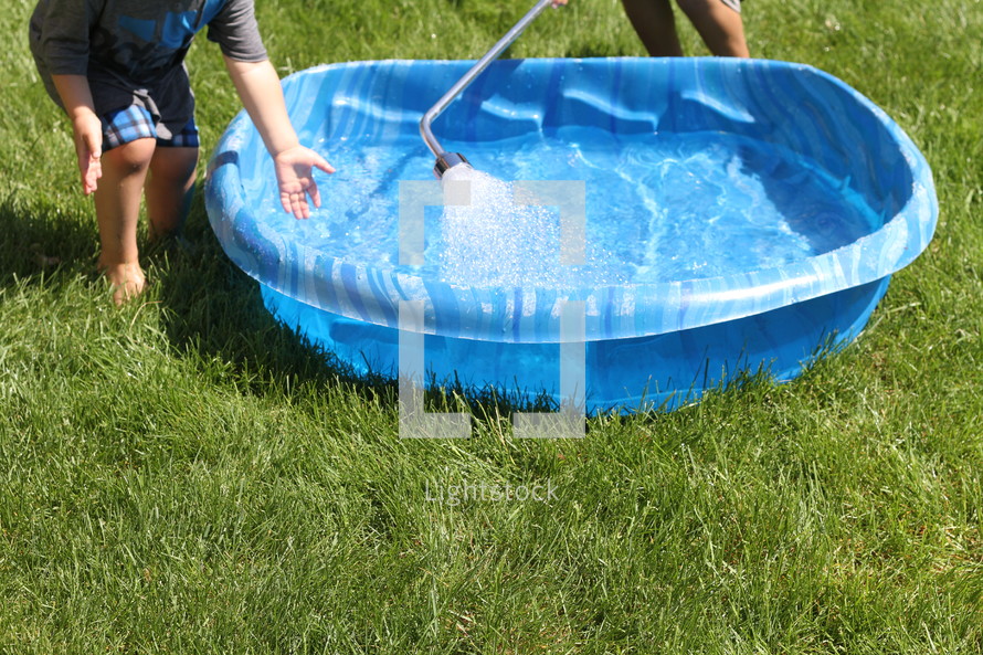 children filling a plastic swimming pool with water 