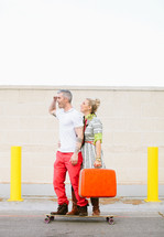 Couple standing on a skateboard holding suitcase