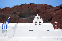 Traditional church with Greece flag in red beach, Santorini