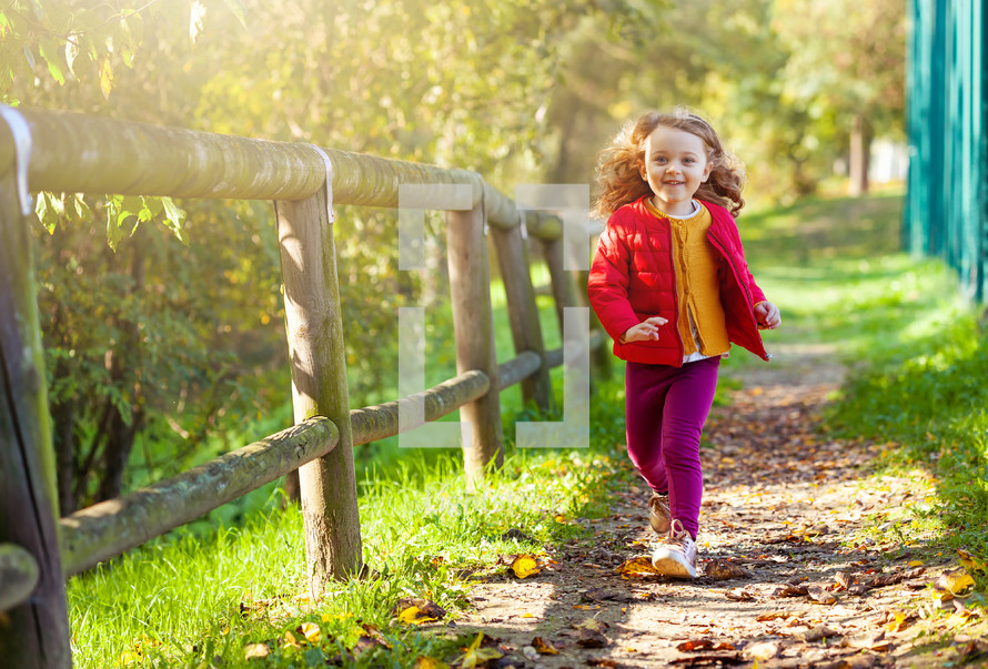 little girl walking in park on a fall day. Female toddler with yellow, red and purple clothing.