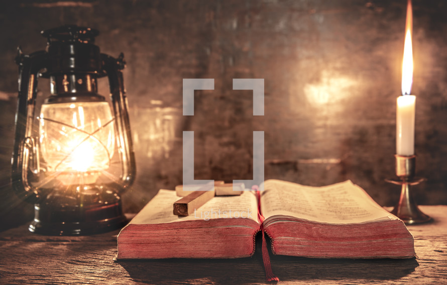 cross on an open Bible and light from an oil lamp and candle