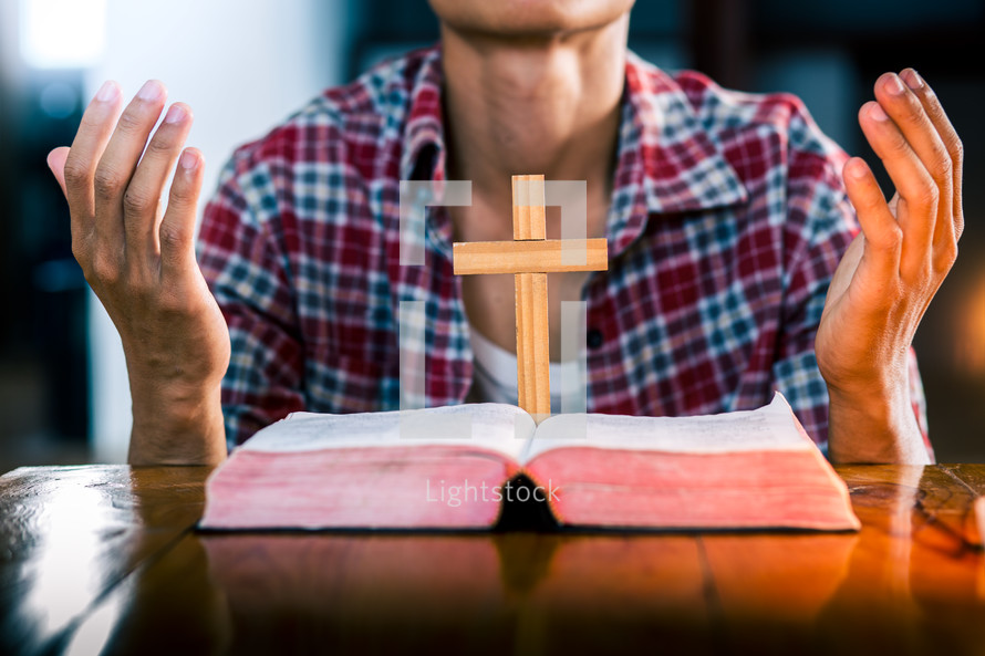 man praying with an open Bible and cross