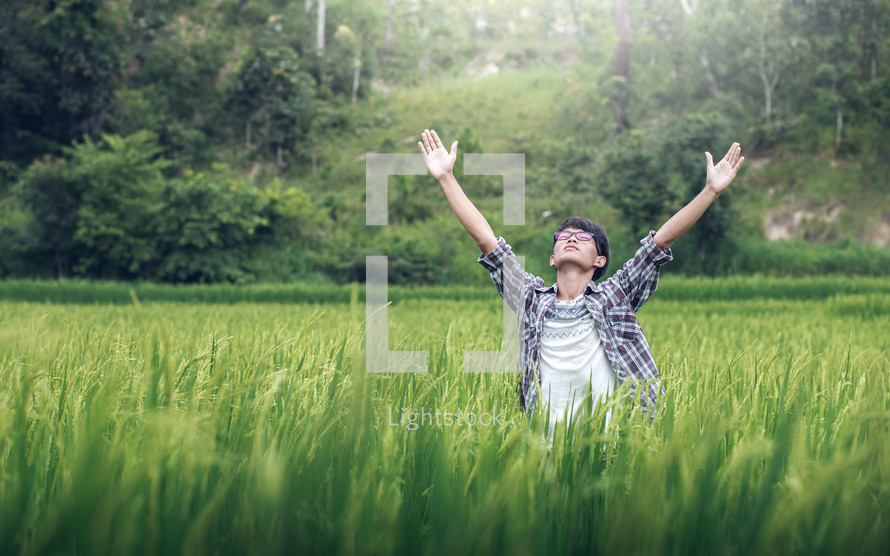 Young male praying with raised hands in a rice field 