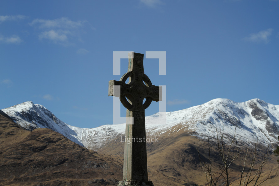 Cross statue outside near snow-covered mountains.