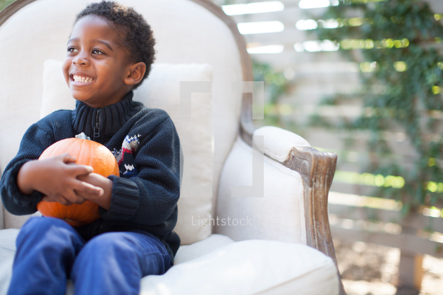 a boy child holding an orange pumpkin 