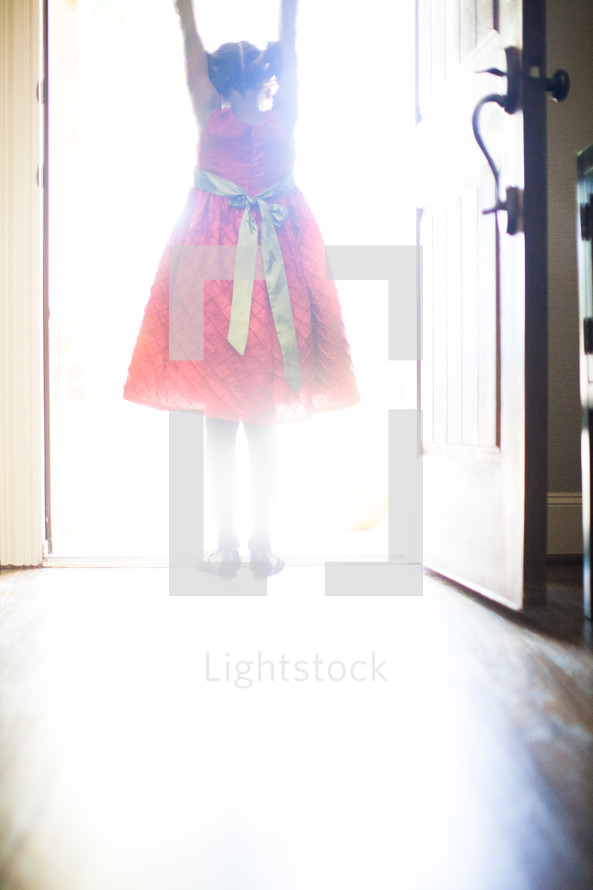 a little girl in a red dress standing in the light from an open doorway